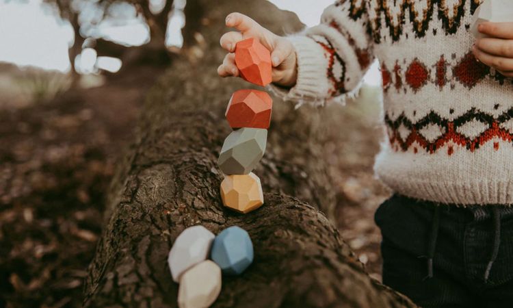 Kind spielt mit Holzspielzeug Balanciersteinen im Wald