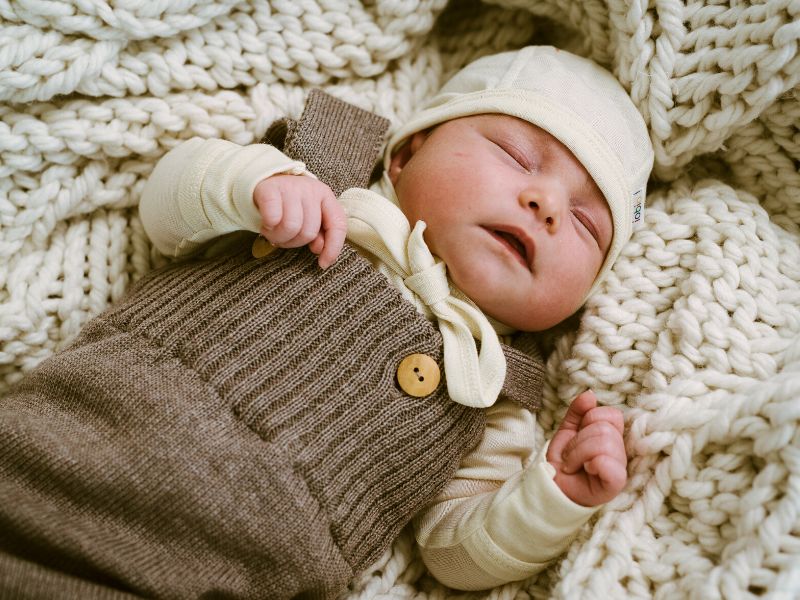 baby in bio kleidung von popolini schläft auf strickdecke, besondere und ökologische geschenke zur geburt