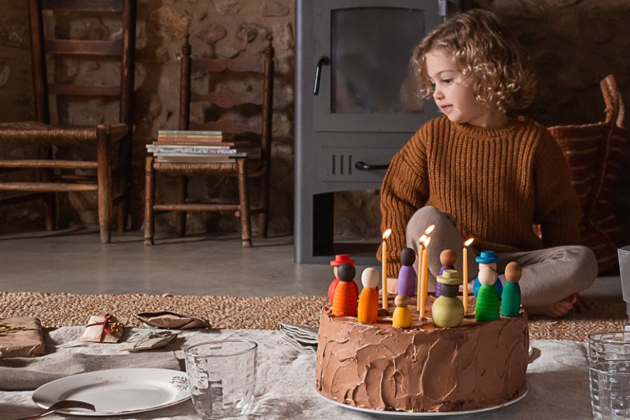 Kind sitzt vor Geburtstagstorte mit Kerzen und bunten Spielfiguren von Grapat