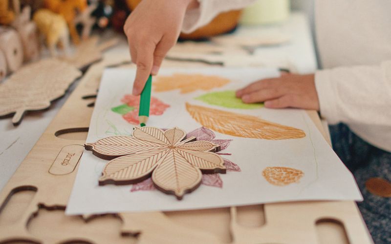 kind malt mit buntstiften blaetter von stuka puka holzpuzzle ab