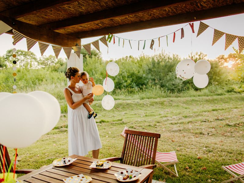 Mama mit Baby auf dem Arm, Geburtstagsdeko im Hintergrund, Geschenke für den ersten Geburtstag